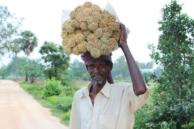 Portrait of smiling vendor carrying brooms while standing against plants