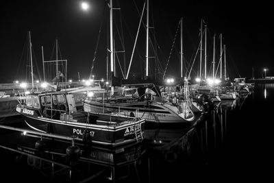 Sailboats moored on harbor against sky at night