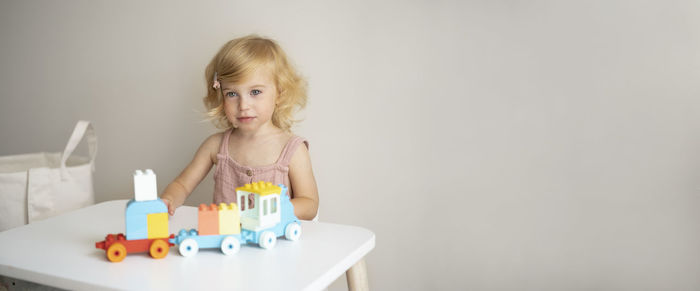 Pretty caucasian 1,2 year old with blond curly hair playing with colourful construction cubes, toys 