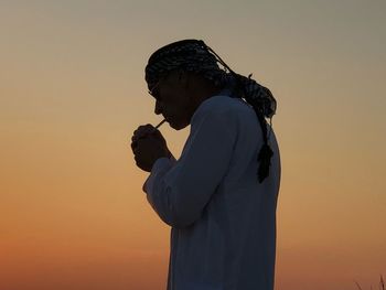 Side view of mature man smoking cigarette against clear sky during sunset