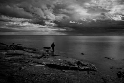 Rear view of man standing at beach against cloudy sky