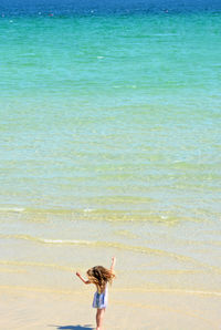 Rear view of woman with arms raised on beach