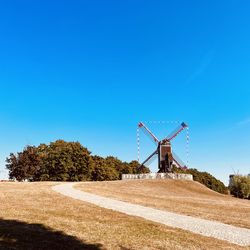 Rear view of windmill standing on hill against clear blue sky