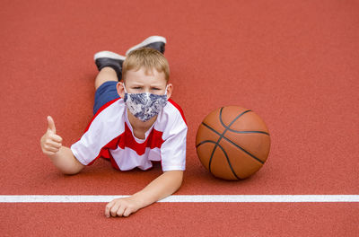 Portrait of boy wearing mask lying on sports court