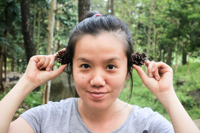 Portrait of smiling woman holding pine cones against trees