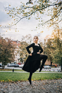 Ballerina dancing in autumn city street, modern ballet dancer in black dress, pointe shoes outdoors