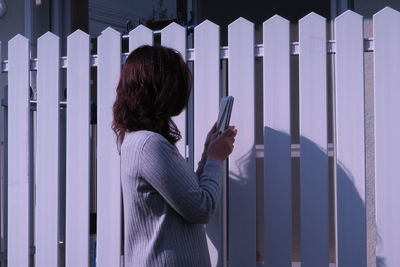 Side view of woman using phone by fence