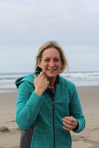 Portrait of smiling woman standing at beach against sky