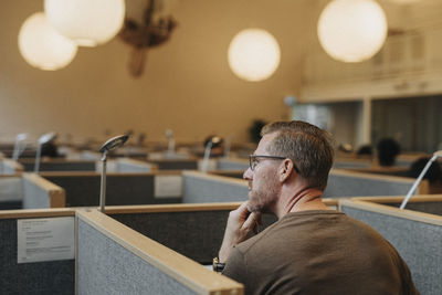 Rear view of thoughtful male professor sitting in library at university