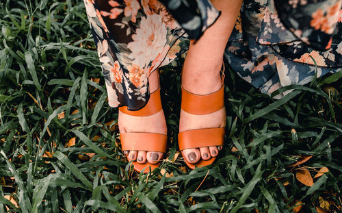 Low section of woman wearing sandal standing on grassy field