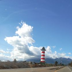 Lighthouse by road amidst buildings against sky