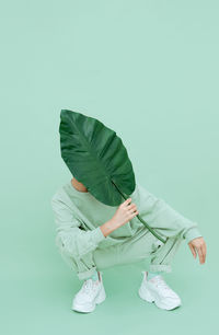 Full length of woman holding leaf crouching on colored background