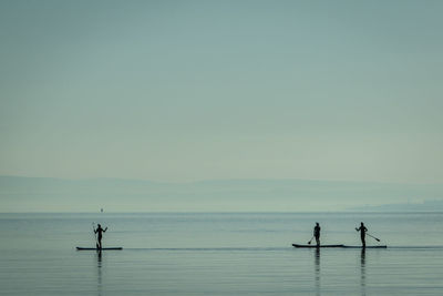 Silhouette people on boat in lake against sky