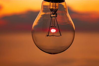 Close-up of light bulb against orange sky