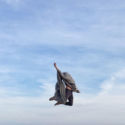 Low angle view of person covered with scarf jumping in mid-air against cloudy sky