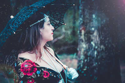 Side view of thoughtful woman wearing pearl necklace with umbrella looking away