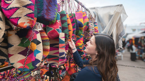 Young latin american woman comparing shigras that hang for sale in the plaza de los ponchos