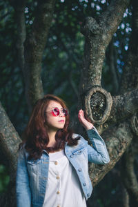 Portrait of young woman standing by tree trunk