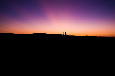 Silhouette couple on landscape against sky during sunset