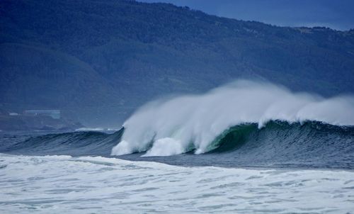 Sea waves splashing on mountain against sky