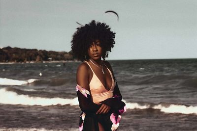 Young woman standing at beach against cloudy sky