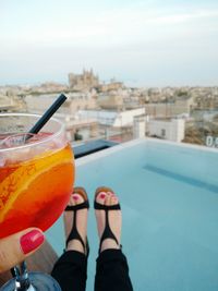 Low section of woman holding drink over swimming pool against sky