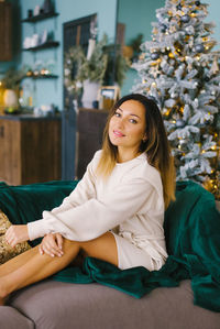 Portrait of a thirty-year-old woman in a cozy home sweater on the sofa near the christmas tree