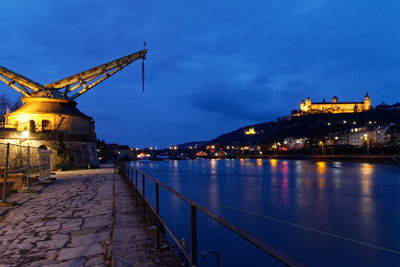 Illuminated buildings by river against sky at night