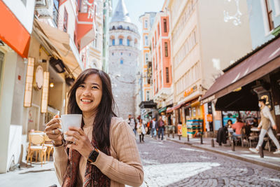 Portrait of young woman standing against buildings