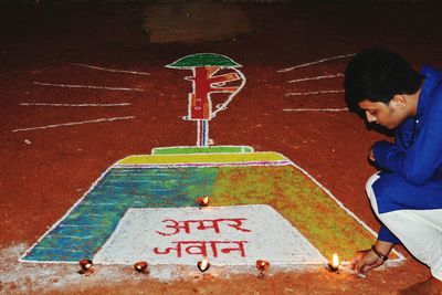 Man crouching while igniting diya from candle by rangoli