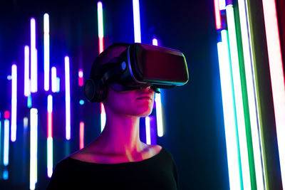 Woman wearing virtual reality simulator near colorful illuminated lights