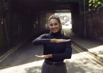 Portrait of woman gesturing while standing on footpath against buildings