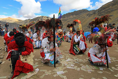 People in traditional clothing dancing on sand against mountains and sky