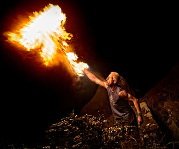 View of man blowing fire at night outdoors