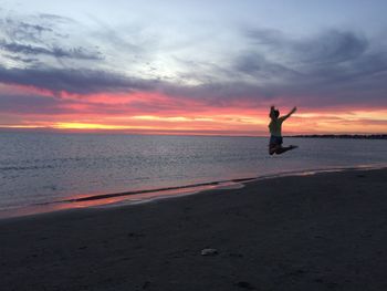 Silhouette man jumping on beach against sky during sunset