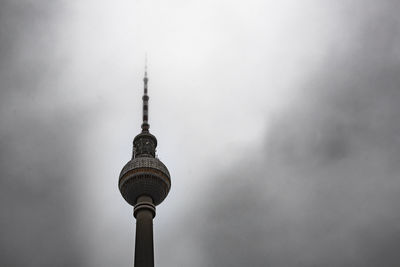 Low angle view of communications tower against cloudy sky