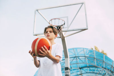Low angle view of boy playing basketball against clear sky