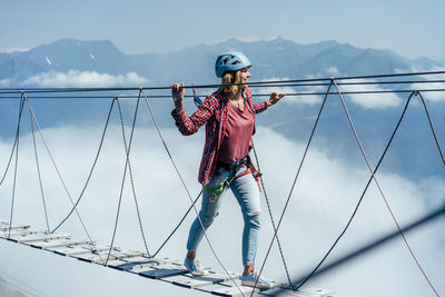 A happy woman walks on a suspension bridge high in the mountains at the level of a cloud. 