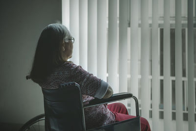 Side view of senior woman sitting on wheelchair at home