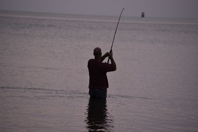 Rear view of fisherman fishing in sea during sunset