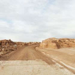 Dirt road leading towards desert against sky