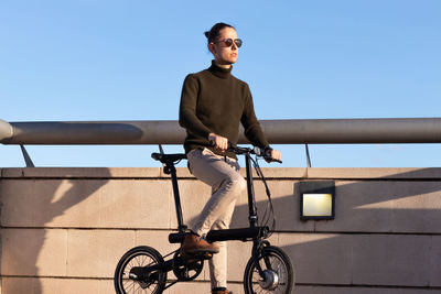 Young man on sunglasses riding an e-bike around the city park under blue sky with sunset light