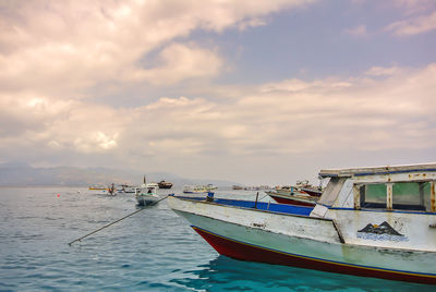 Boats in sea against cloudy sky