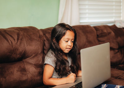 Cute girl using laptop while sitting on sofa at home