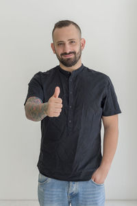 Portrait of young man gesturing thumbs up sign against white background