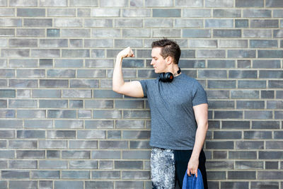 Young man flexing muscles while standing against brick wall