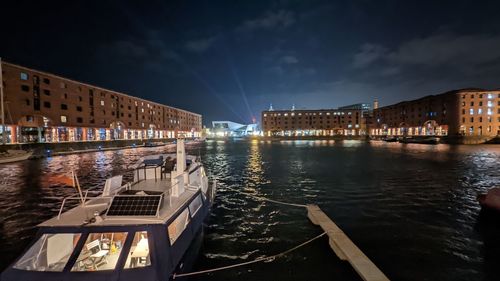 Illuminated buildings by river against sky in city at night