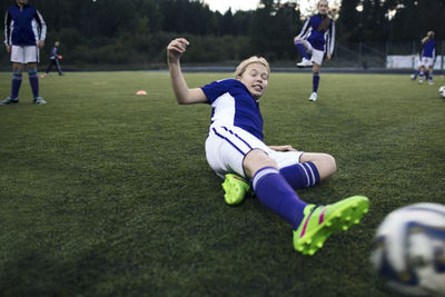 Girl sliding on grass at soccer field during training