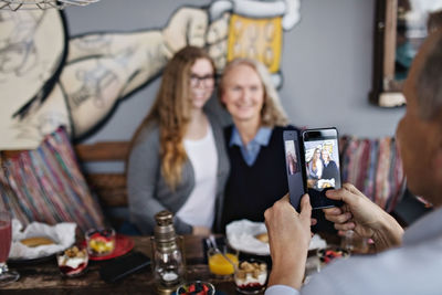 Mature man photographing women through smart phone at restaurant