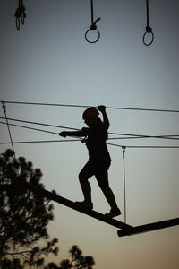 Low angle view of silhouette girl walking on rope against sky